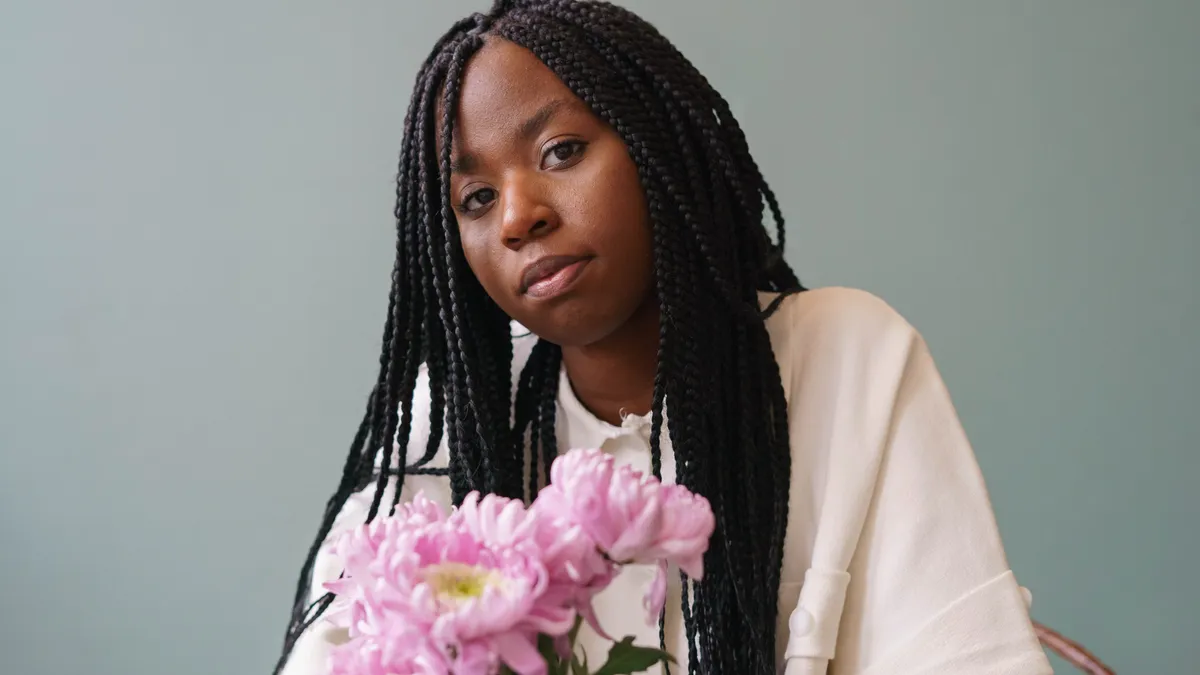 A Black person holds flowers and looks at the camera