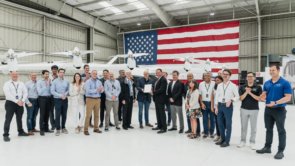 Large group of people in front of an eVTOL aircraft inside a building.