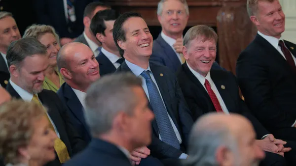 Seated men in suits and one woman laughing.