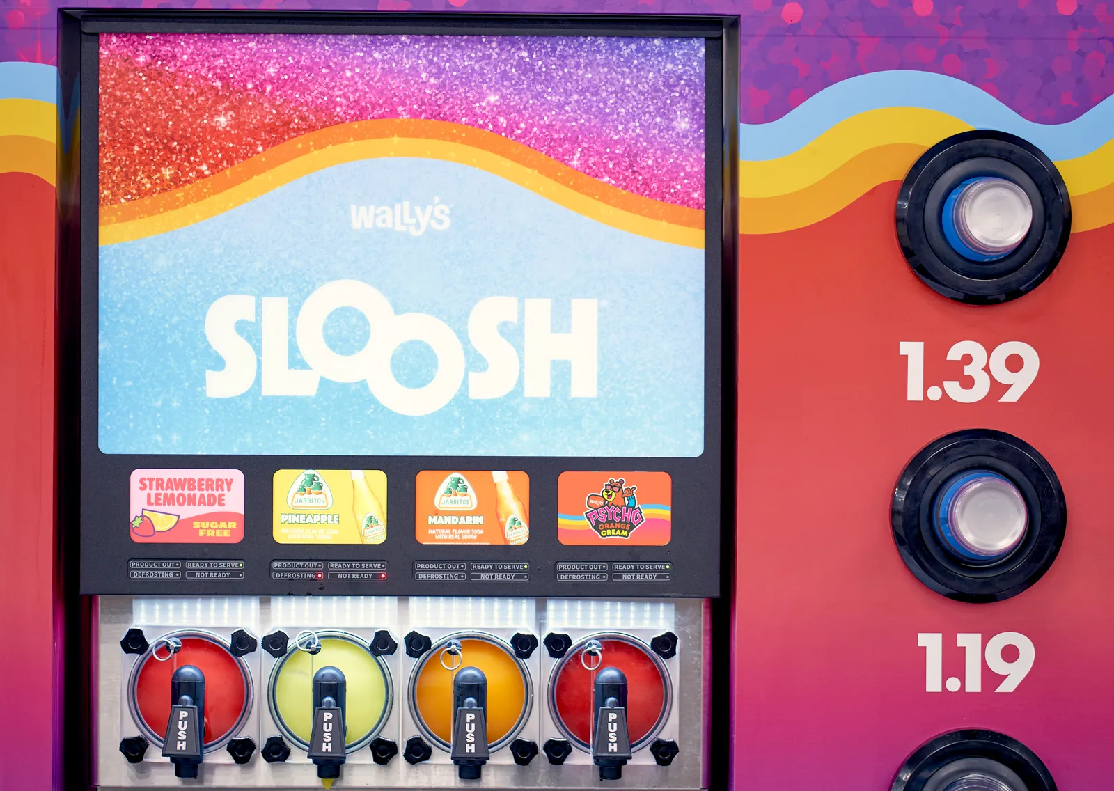 A photo of a beverage dispenser with four spigots and three sizes of cups available along the right side. The machine says &quot;Wally&#x27;s Sloosh&quot;  at the top and lists flavors strawberry lemonade, pineapple, mandarin and orange cream above the spigots.