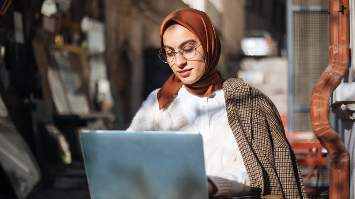 Young woman sitting at sidewalk cafe and using Laptop