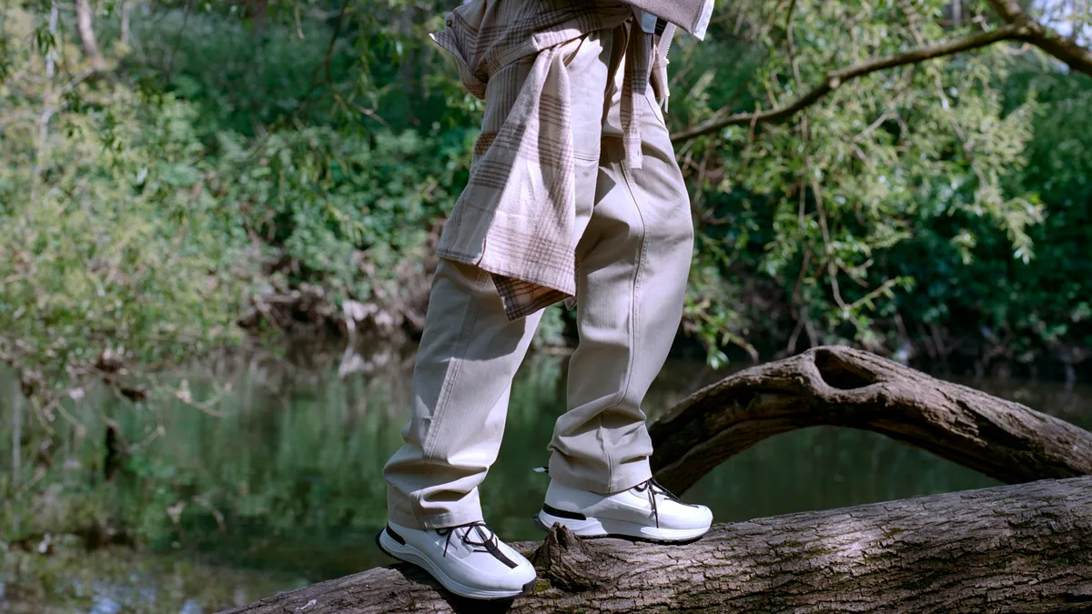 A model poses in outdoor attire and white sneaker while standing on a large tree branch