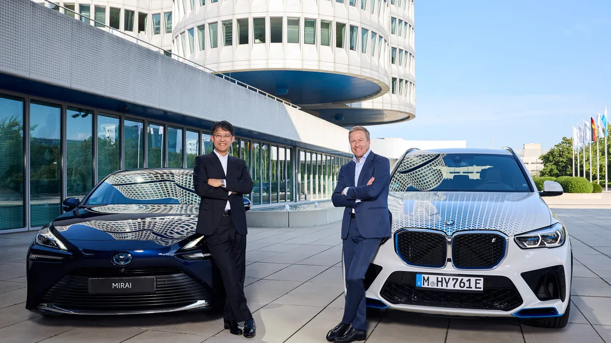 Pictured are Toyota Motor Corp. president Koji Sato (left), and Oliver Zipse, Chairman of the Board of Management of BMW, posing in front of a Toyota and BMW vehicle.