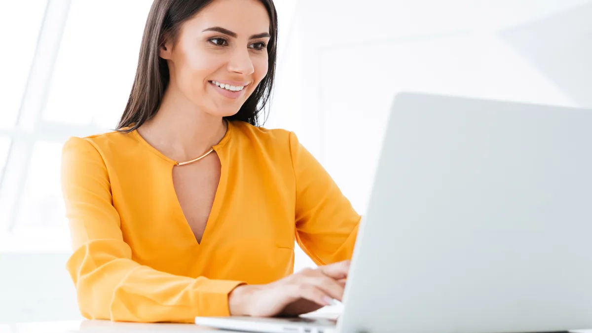 Business woman in orange shirt using laptop computer and sitting by the table in office