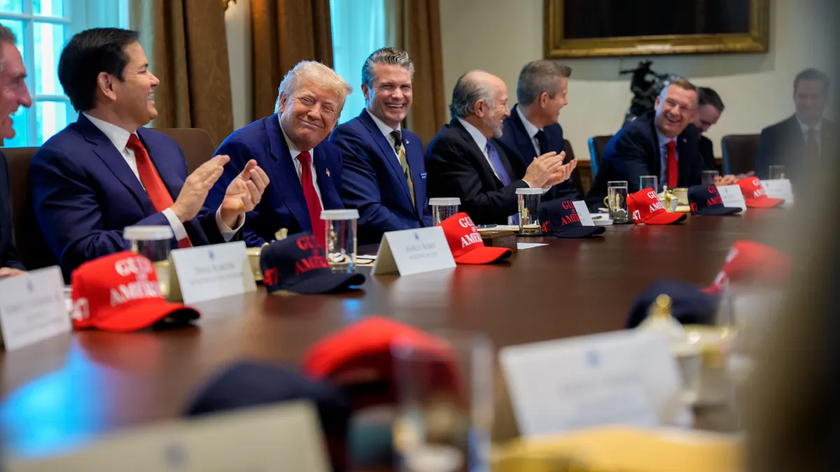 Men in suits around a table with red ballcaps on the table.