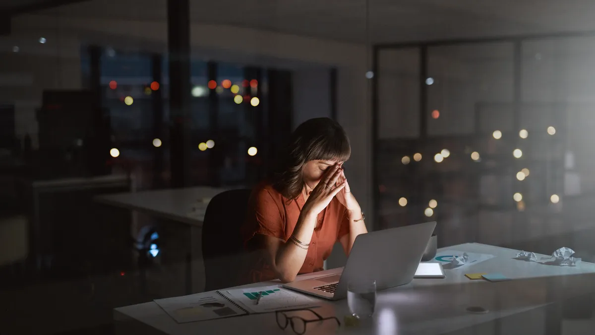 A person clasps their head at their desk, in an office