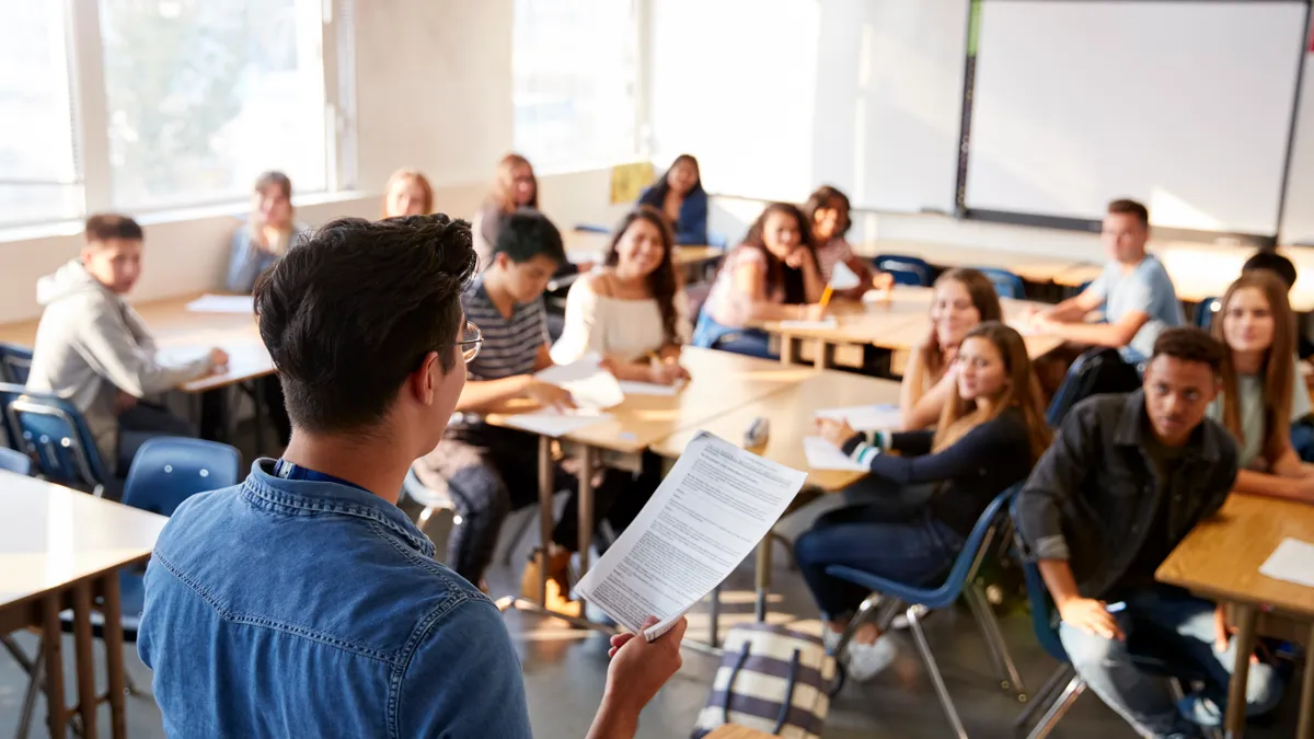 A view from behind a teacher instructing in front of a class of high school students.