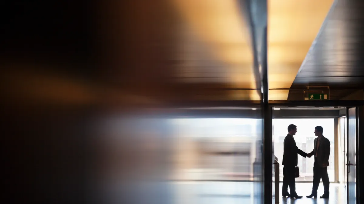 Two men shake hands at the end of a long hallway
