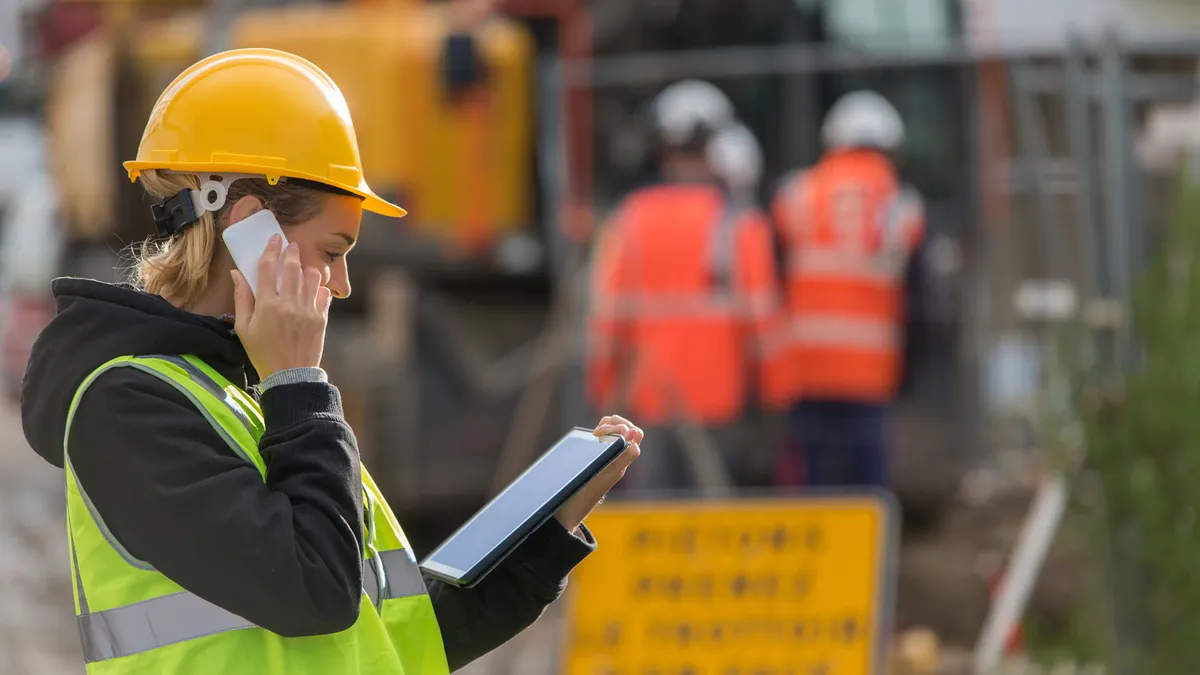 Engineer manager woman wearing safety helmet using digital table in construction site while standing