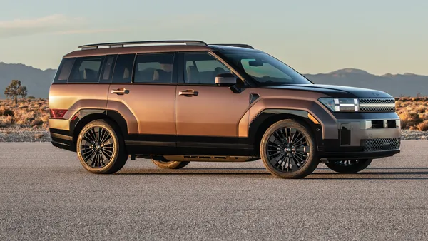 A right side view of a bronze-colored Hyundai Santa Fe SUV outdoors in a desert environment with hills in the background.