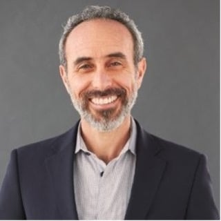 A headshot of a bearded person, smiling.