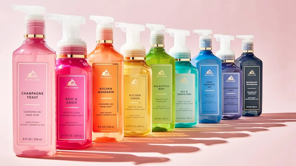 Nine bottles of hand soap are lined up and cast their shadows on the pale pink background.