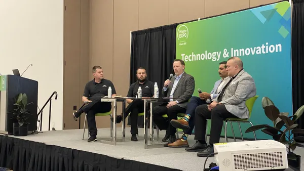 Five men sit around a table on a podium while one in the center speak into a microphone. A backdrop behind them has the Waste Expo logo and the words "Technology & Innovation."