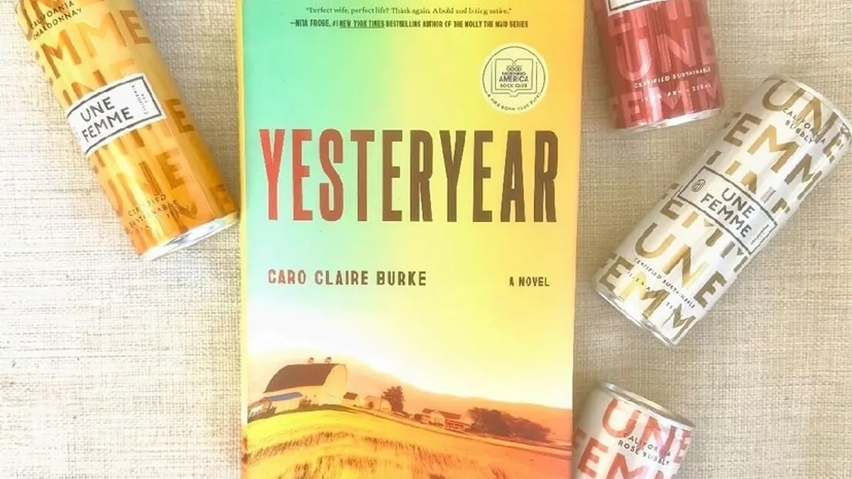 A copy of "Yesteryear" by Caro Claire Burke surrounded by cans of Une Femme wine on a woven tan background.