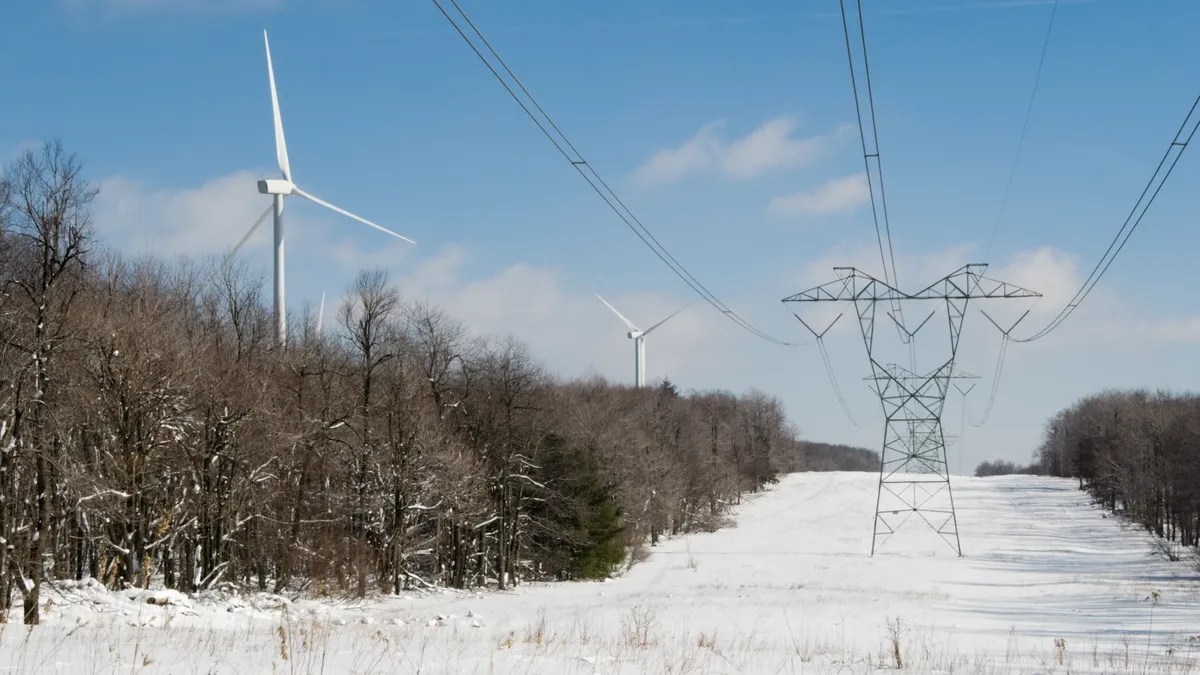 Transmission lines in the winter with wind turbines in the background.