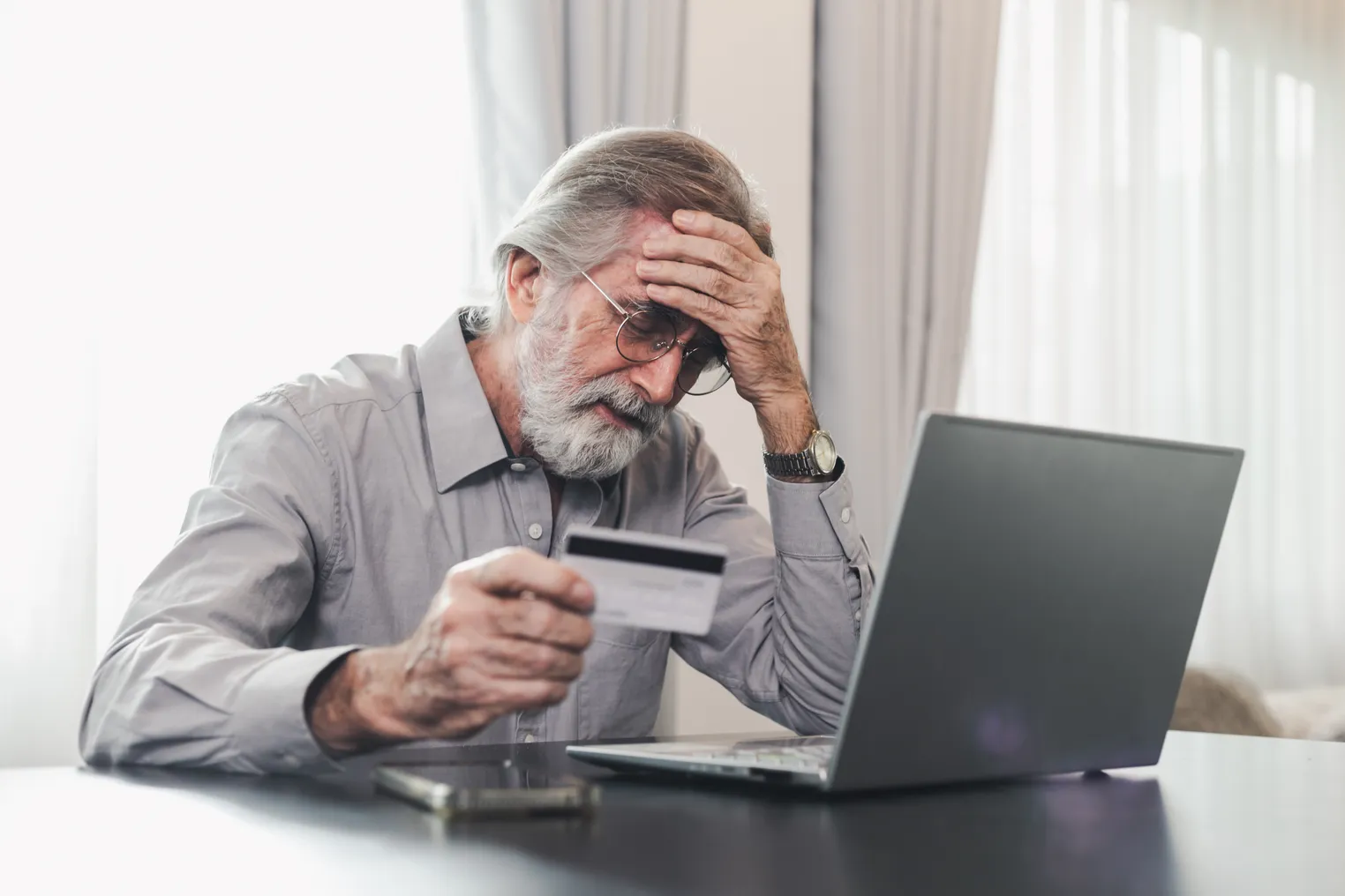 Man leans over laptop with head in hand looking at credit card.