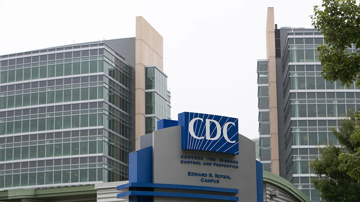 Sign for the Center for Disease Control in Atlanta stands in front of a tall glass building.