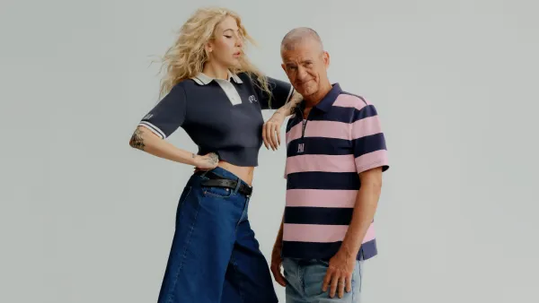 A woman stands on a box next to a man and leans on his shoulder. Both wear casual attire.