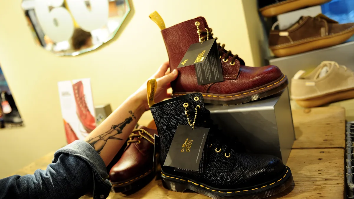 A close up of a person's arm grabbing for a Dr. Martens boot on display at a store.