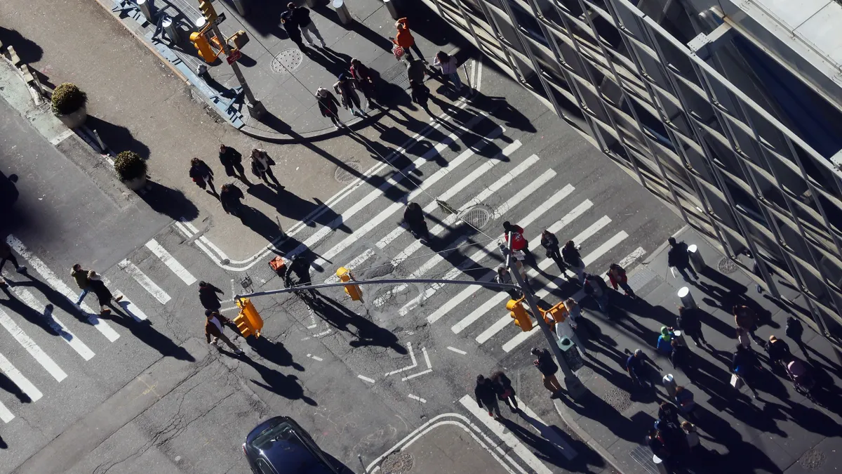 Overhead view of dozens of people crossing streets in different directions.