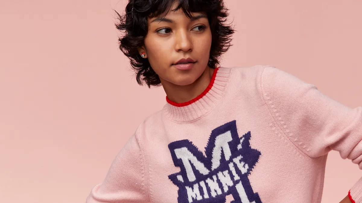 A person wearing a pink sweater that says "Minnie" and a striped skirt with ears on their head.