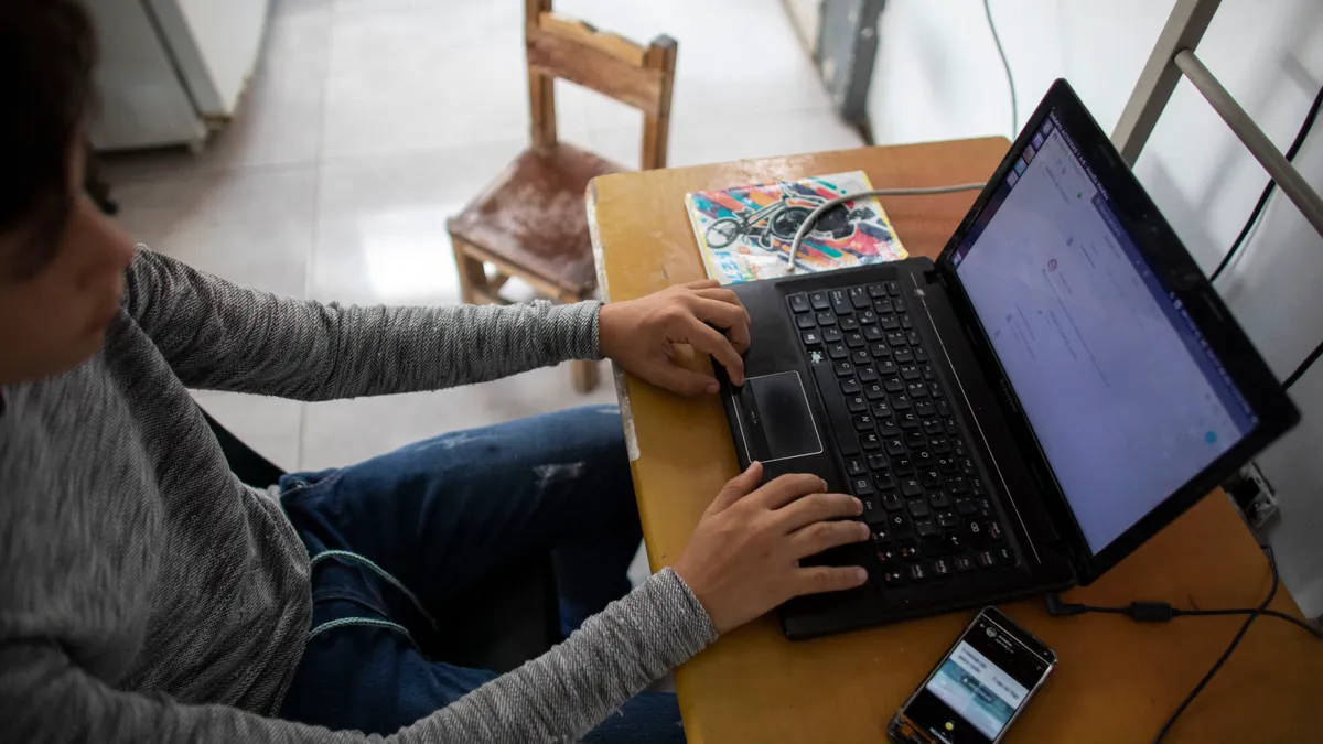 A teenager sits in front of a computer and a phone on a desk.