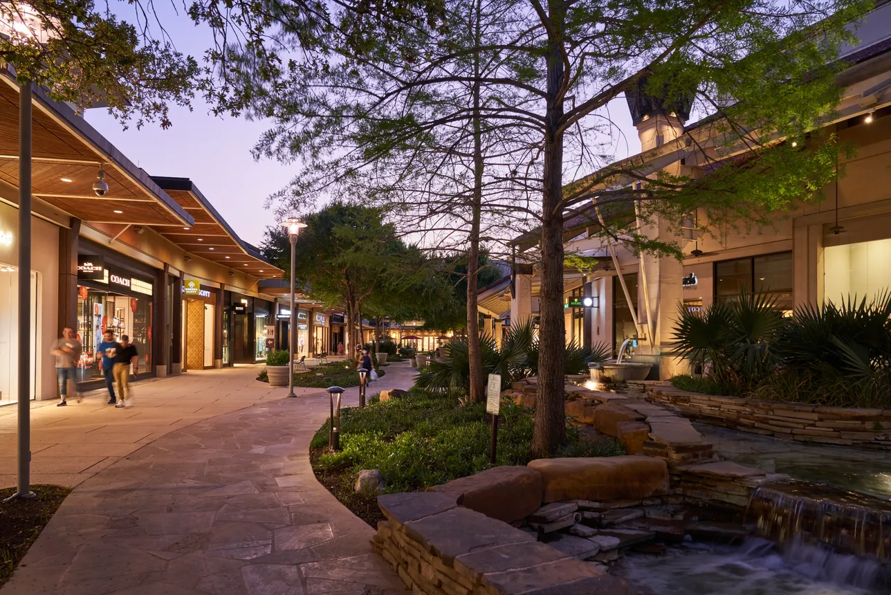 People walking through a shopping center with stores and trees.