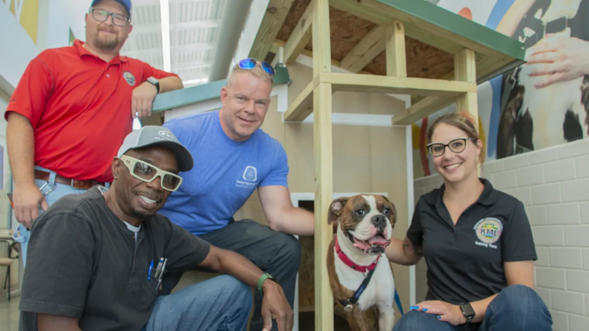 Four volunteers surround a dog on the porch of its doghouse.