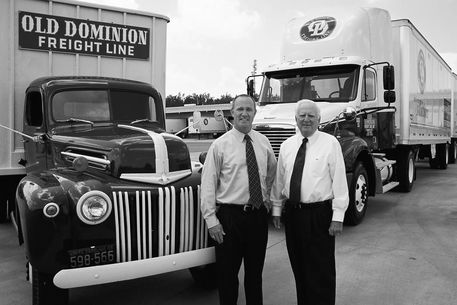 Two people stand in front of two trucks.