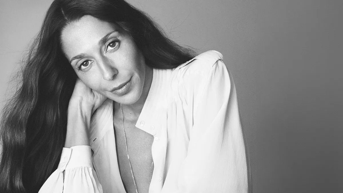 Chemena Kamali, wearing a white blouse and with long brown hair, looks into the camera in a black-and-white headshot.