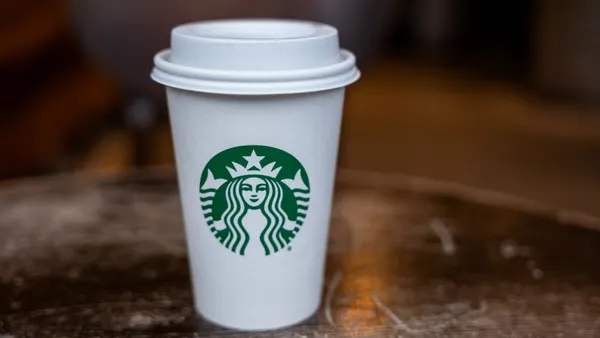 An image of a white coffee cup on a table. The coffee cup hasa green logo for Starbucks.