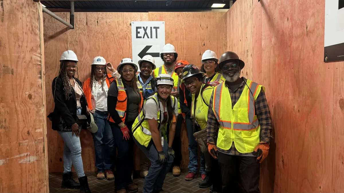 A group of people in construction safety gear pose and smile for a photograph.
