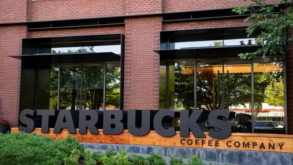 A photograph of a black sign that says "Starbucks Coffee Company" in front of a brick building.