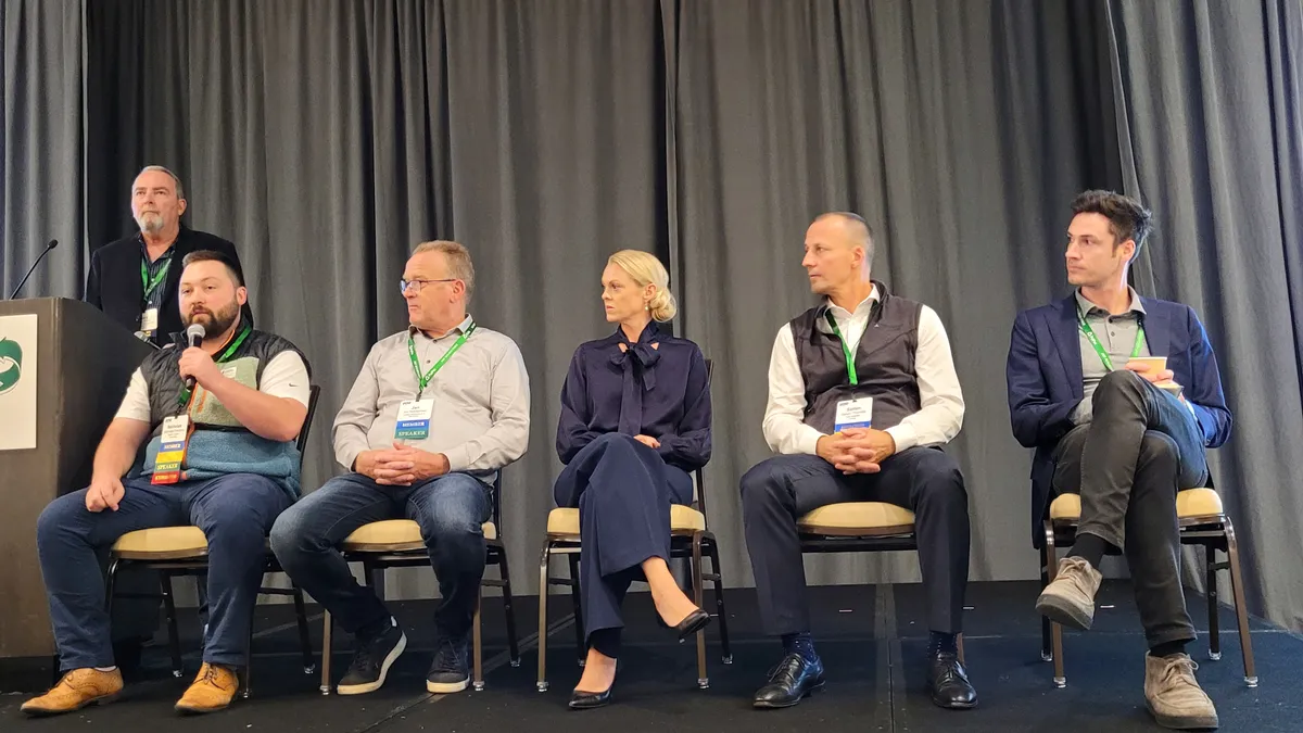 Five people sit on chairs on a stage during a panel discussion at a conference.