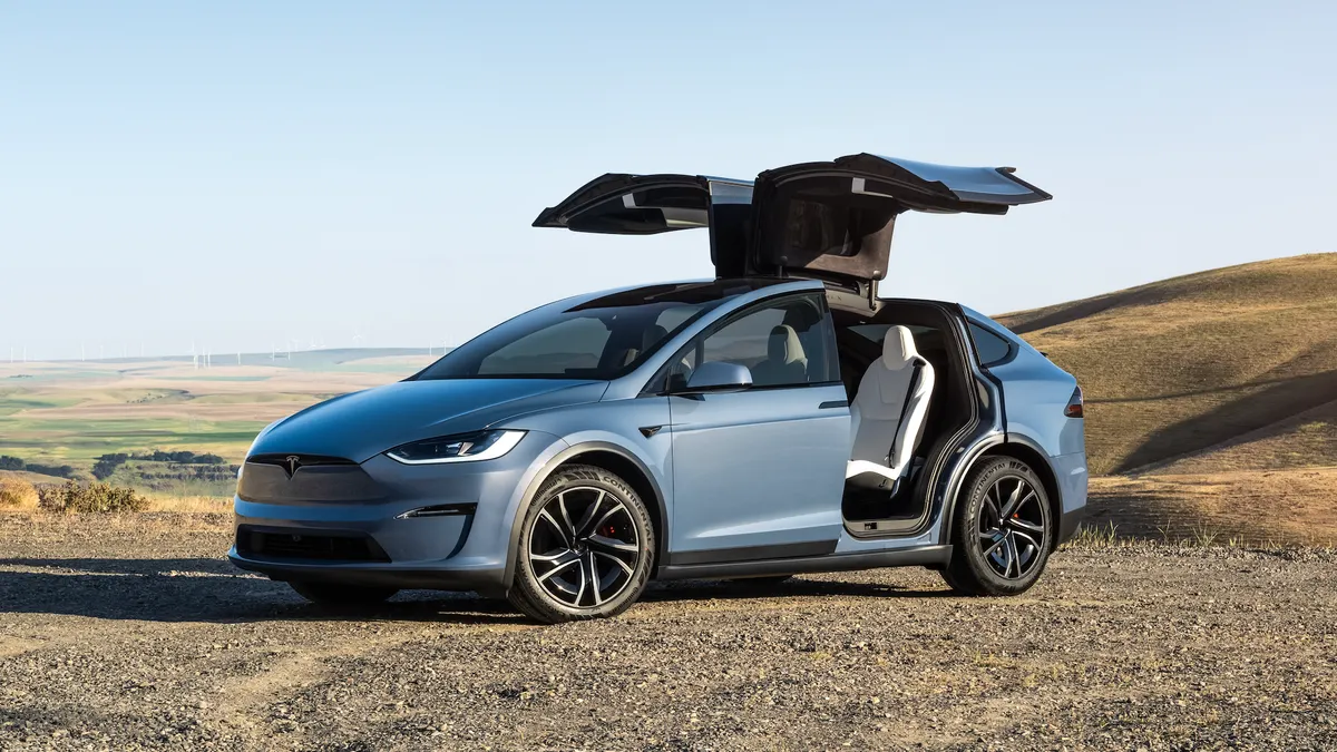 A blue Tesla Model X parked outdoors with its rear gull-wing doors fully opened.