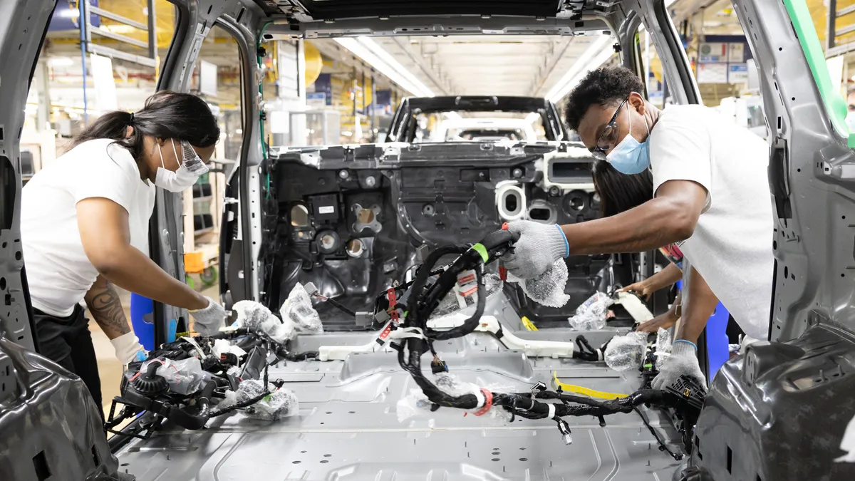 Two Employees at the Warren Assembly Plant install the wire harness in the all-new Wagoneer on the assembly line.