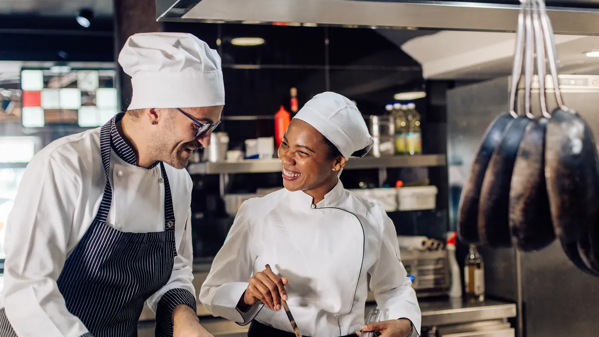 Two chefs smiling and cooking in a restaurant kitchen.