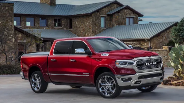 A red 2024  Ram 1500 pickup parked in front of a stone, two-story building.