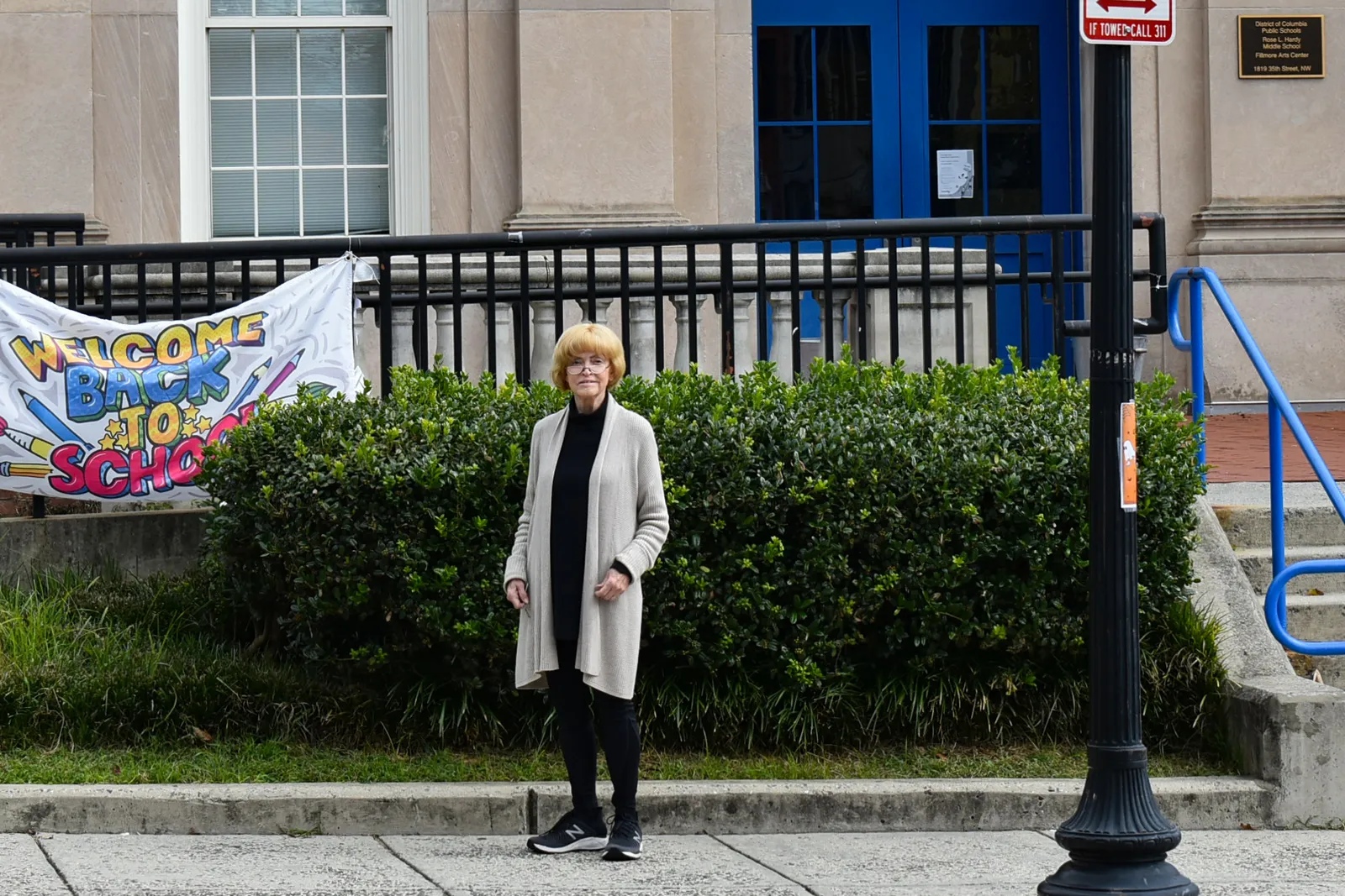 A person stands on a sidewalk in front of a school building