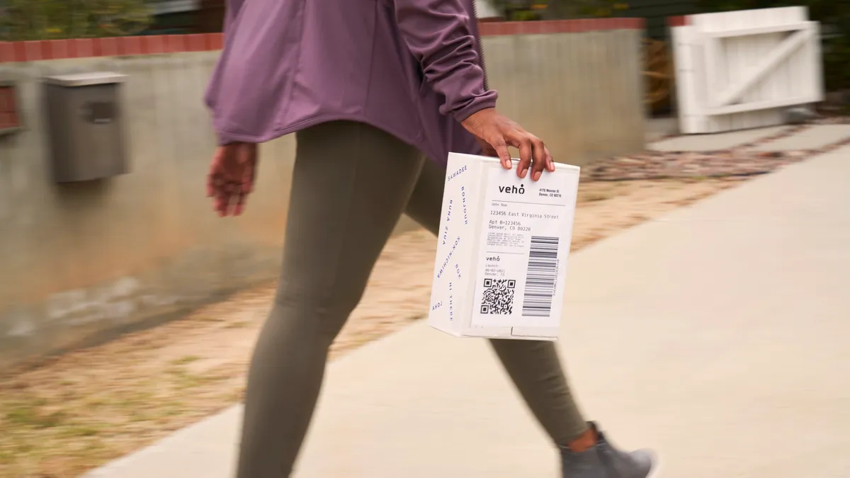 A person carries a package. The package reads, "Veho"