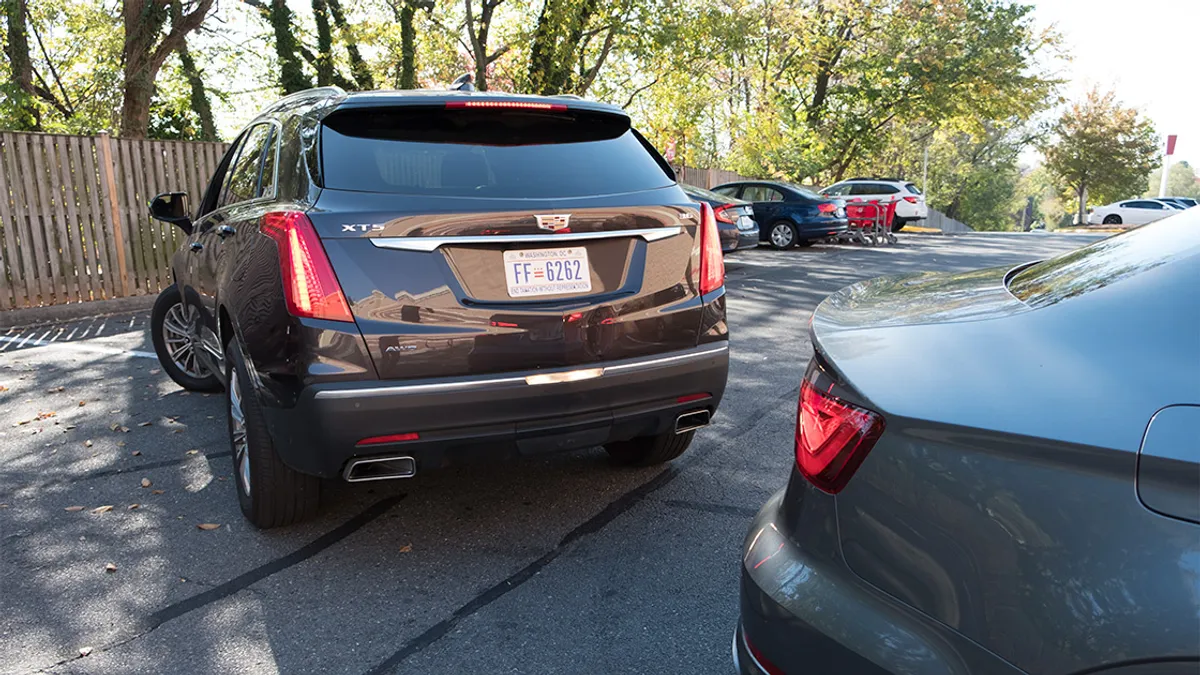 A black Cadillac XTS SUV backing up near another vehicle in a parking lot with trees in the background.