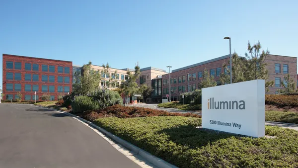 A sign that says Illumina is on a curb in front of red brick buildings.