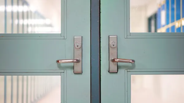 A school building's door is closed. Through the door's windows a hallway with lockers appears in the background.