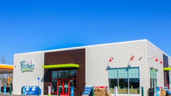 A photo of the exterior of a convenience store on a bright, cloudless day. The walls are gray and brown and a blue logo says "Freshies" on the wall