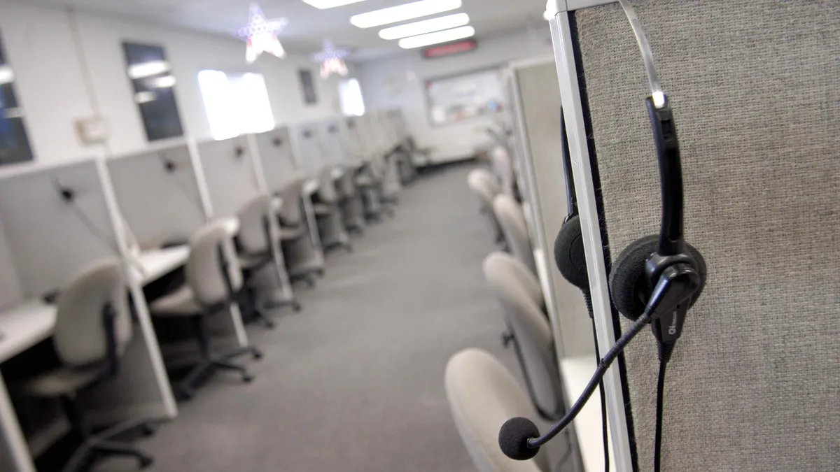 A headset hangs on an empty call center cubicle