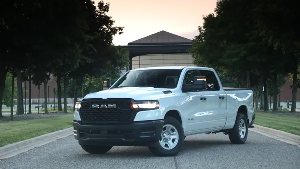 A white 2025 Ram 1500 Tradesman pickup parked outdoors with green trees in the background.