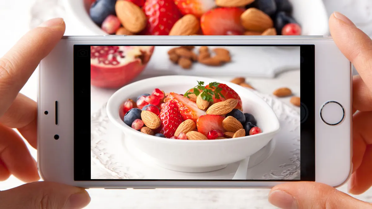 Cropped picture of a bowl of fruits and almonds taken by a person on a white iphone.