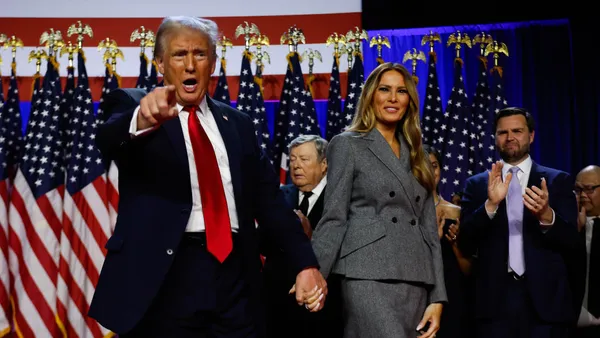 Donald Trump points to his supporters while holding Melania Trump's hand.