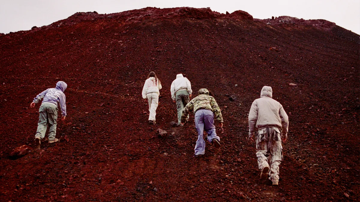 Four people in outdoor gear climb up a dirt mountain, as seen from behind.