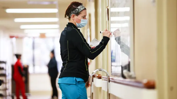 A person wearing scrubs writes on a white board.